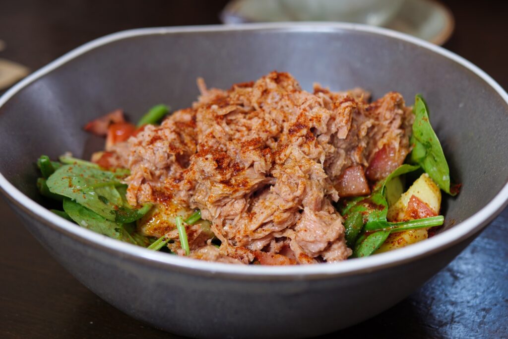 Close up photo of a tuna salad with potatoes, tomatoes, spinach and green beans sprinkled with smoked paprika seasoning and served in a grey bowl